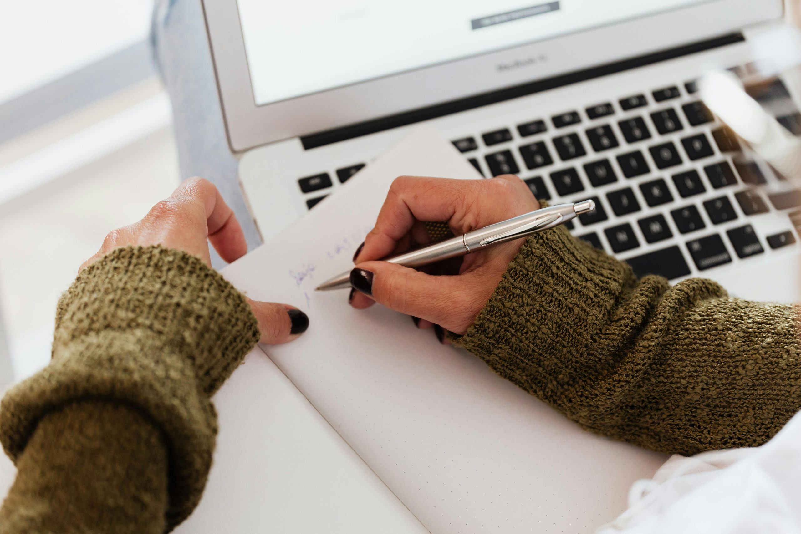 Girl Writing On Notepad While Working On MacBook